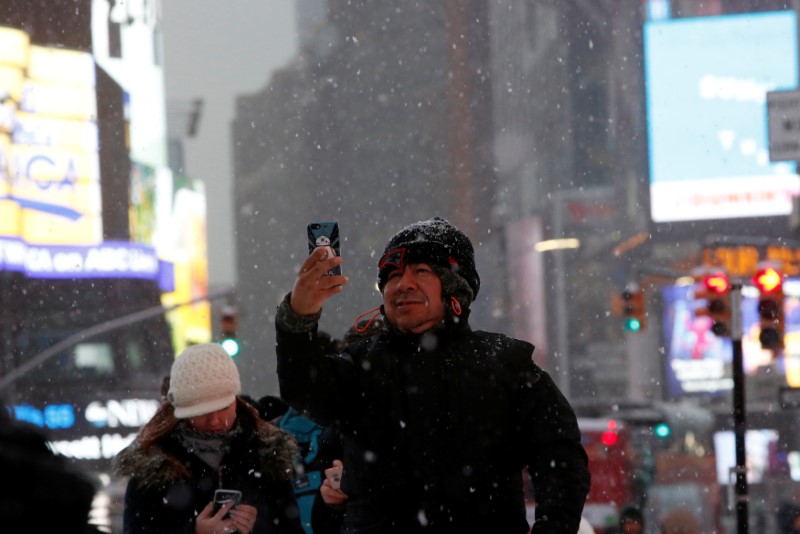 A man takes a photo in Times Square during morning snow in Manhattan, New York City, U.S. December 17, 2016.  REUTERS/Andrew Kelly