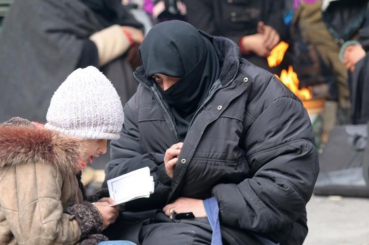 A woman sits with her child reading the Koran while waiting to be evacuated with others from a rebel-held sector of eastern Aleppo, Syria December 17, 2016. REUTERS/Abdalrhman Ismail