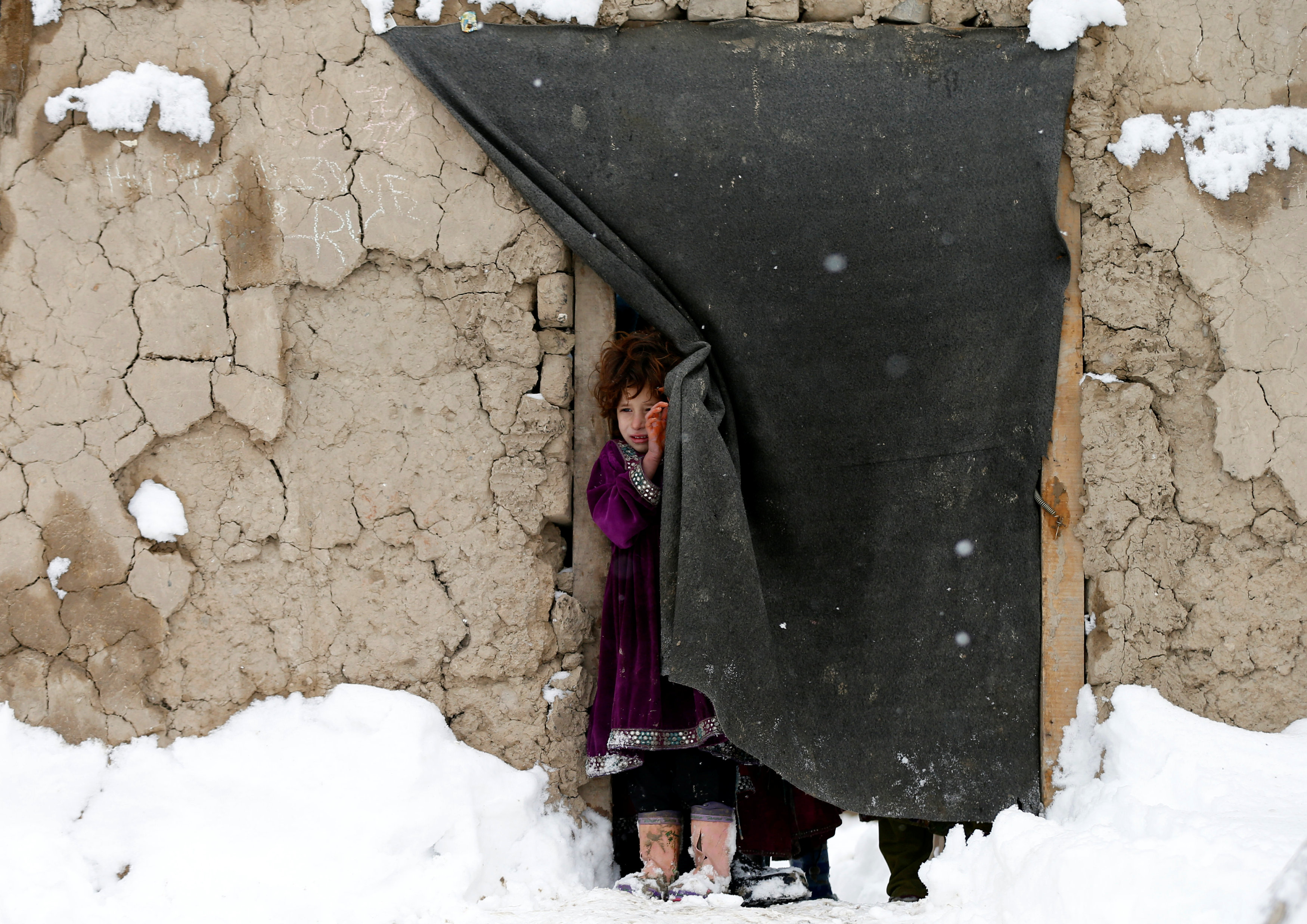 An internally displaced Afghan girl stands at the door of her shelter during a snowfall in Kabul, Afghanistan February 5, 2017. REUTERS/Mohammad Ismail