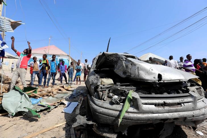 Civilians stand near a car destroyed in a suicide bomb explosion at the Wadajir market in Madina district of Somalia's capital Mogadishu, February 19, 2017. REUTERS/Feisal Omar